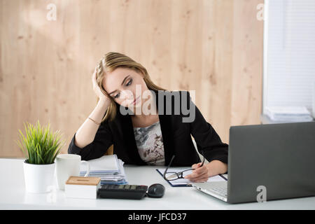 Tired business woman sitting at her working place. Overwork, working overtime and stress at work concept. Stock Photo