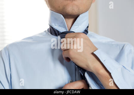 Handsome businessman preparing to official event, straighten tie. New job interview, self motivation for confidence, trying fashionable necktie knot,  Stock Photo