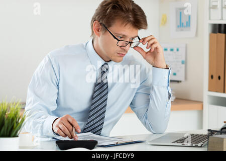 Portrait of bookkeeper or financial inspector adjusting his glasses making report, calculating or checking balance. Home finances, investment, economy Stock Photo