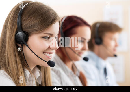 Portrait of call center worker accompanied by her team. Smiling customer support operator at work. Help and support concept Stock Photo