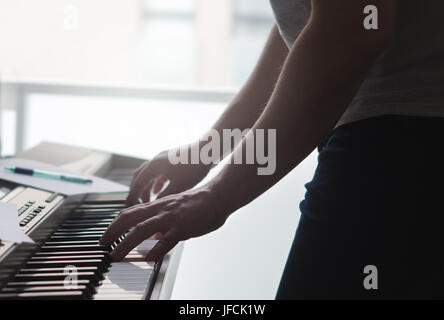 Man play piano standing. Talented musician and pianist practice and train skills by the window. Note paper and pen on the instrument. Stock Photo