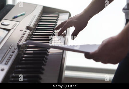 One single finger pressing key on piano. Man looking at paper notes and training a new song or melody from the sheet music. Pianist composing new work Stock Photo