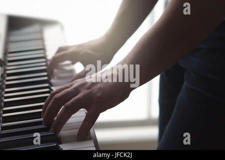 Man playing piano standing in home studio. Ambient mood with sun light. Close up of male hands on keys of electronic keyboard. Person plays music. Stock Photo