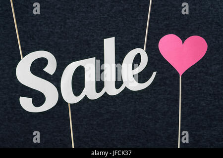 Sale text cut from cardboard paper on wooden stick and dark background. Marketing material for valentine's, women's or mother's day special offer. Stock Photo
