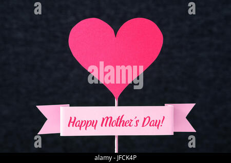 Happy Mother's Day text on a ribbon and red heart shape cut from cardboard on wooden stick. Nice simple greeting design for Mothers Day card. Stock Photo