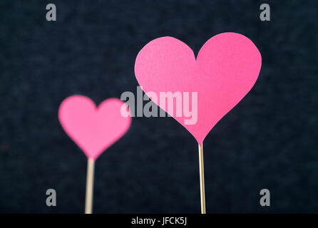 Two romantic hearts cut from cardboard or paper on wooden stick and dark background. Beautiful, handmade pink red love shapes. Stock Photo