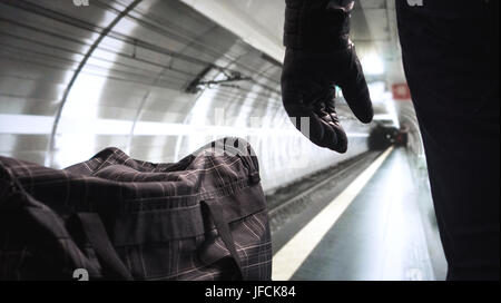 Terrorist in underground subway. Terrorism in empty metro platform. Security threat. Bomber standing next to his black bomb bag planning a strike. Stock Photo