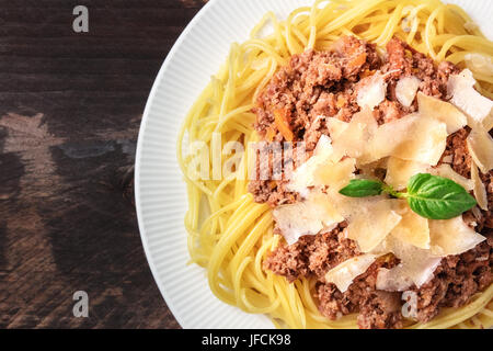 An overhead photo of a plate pf bolognese pasta with grated parmesan cheese and fresh basil leaves, on a dark rustic texture with a place for text Stock Photo