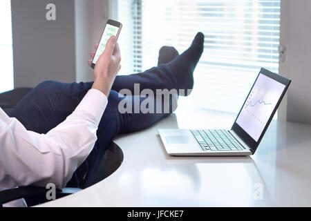 Successful business going well. Businessman laying in office with feet on table while income is rising and getting easy money. Stock market going up. Stock Photo