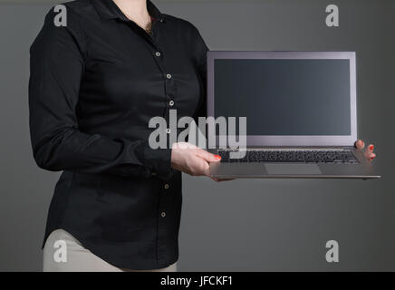 Business woman presenting a software or showing an application. Girl holding laptop with dynamic pose and black collared shirt. Empty screen. Stock Photo