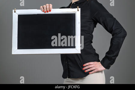 Energetic and sporty young girl holding chalkboard with one hand. Business woman or waitress in a restaurant with black collared shirt. Stock Photo