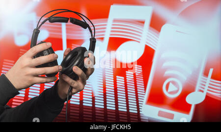 Close up of male hands holding large headphones in front of an abstract note and equalizer background. Man putting earphones on and listen to music. Stock Photo