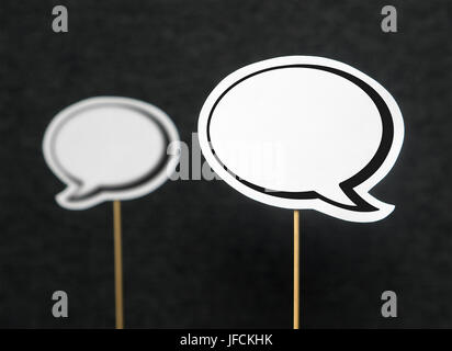 2 blank speech bubbles on a dark black background. The other speech balloon blurred. Chat bubble cut from paper with wooden stick. Discussion, protest Stock Photo