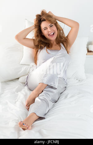 Young pretty woman lays in her bed in the morning, stretches hreself, tousles her hair and makes funny faces showing her tongue. Morning leisure Stock Photo