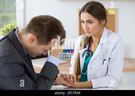 Female medicine doctor holding business man hand for encouragement telling him bad news. Immediate relative loss, stress, headache and medical service Stock Photo