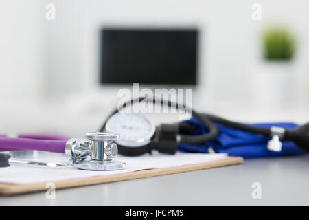 Medicine doctor's working place. Close up view. Focus on stethoscope laying on desktop. Computer monitor and manometer on background. Healthcare and m Stock Photo