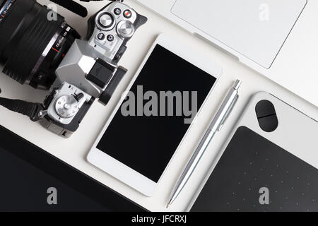 Top view of designer, blogger or photographer working table. Graphic tablet, tablet pc, laptop, smartphone and photo camera laying on white table. Stock Photo