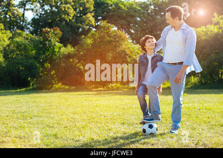 Hobbies through generations. Handsome happy genuine man enjoying an active weekend and dedicating it to his family while teaching his son some footbal Stock Photo