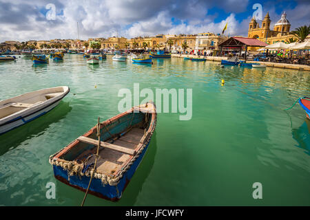 Marsaxlokk, Malta - Traditional colorful maltese Luzzu fisherboats at the old market of Marsaxlokk with green sea water, blue sky and palm trees on a  Stock Photo