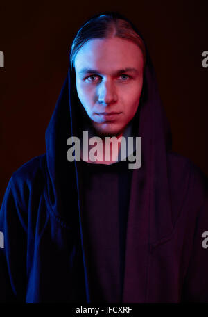 Young blond mystic man in hood on black Stock Photo