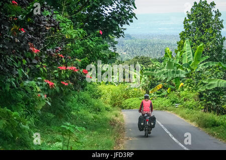 Female cyclist cycling through tropics in Lombok, Indonesia Stock Photo