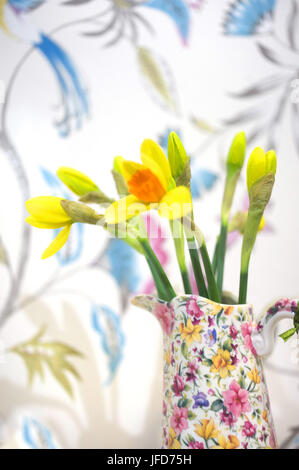 Daffodils in jug with floral wallpaper behind Stock Photo