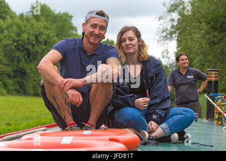 Couple sitting on roof of wide beam passenger boat barge along Kennet and Avon Canal at Kintbury, West Berkshire in June Stock Photo