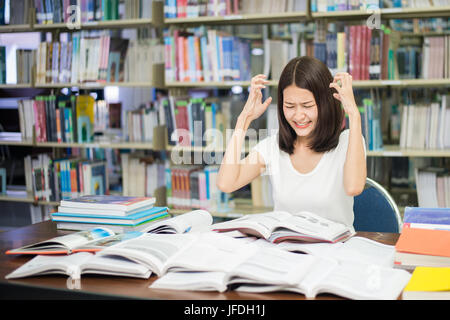 Young Asian student under mental pressure while reading book preparing examination in library at university. Asian student looking stressed. Stock Photo