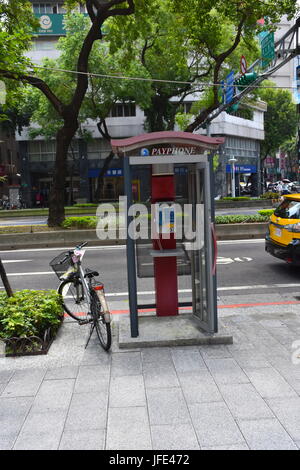 A bicycle parked next to a public phone booth on the curb in Taipei, Taiwan along the street. Stock Photo