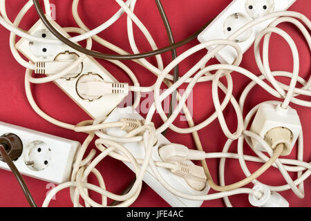 Cable chaos clutter from multiple electric wire extension cords and multi-contact plugs on red background Stock Photo
