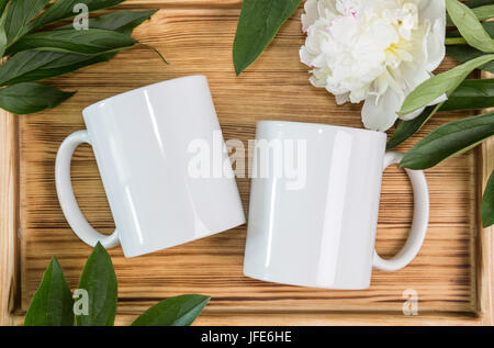 Two white mugs, cups wedding mockup. Peony, green leaves, wooden background. Summer gifts, boho style Stock Photo