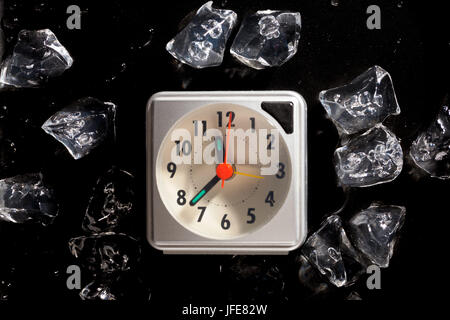 Frozen in time concept with ice cubes and a clock and melting water drops on a dark background Stock Photo