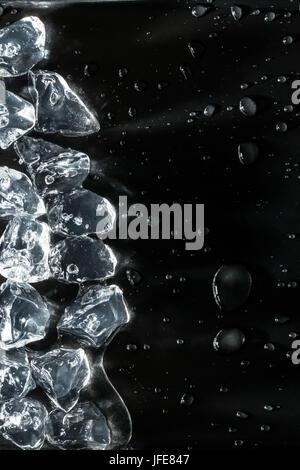 Ice cubes melting on edge of image, with water droplets on a dark background Stock Photo