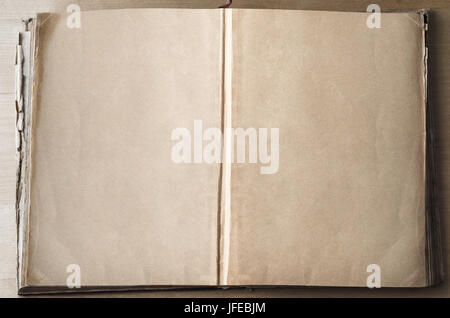 An old vintage book on a wooden table, opened out from it's centre to expose blank, parchment coloured pages. Stock Photo