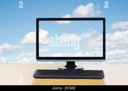 Conceptual image of cloud computing.  Computer monitor and keyboard on light wood table facing the viewer,  in front of fluffy white clouds on a blue  Stock Photo