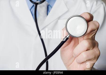 Close up of a Doctor's hand, holding a stethoscope outstretched towards the viewer.  Doctor's white coat provides space to the left side of frame. Stock Photo