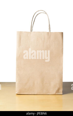 An unbranded brown paper carrier bag with twisted handles on a light wood table with white background, facing front with empty space for text. Stock Photo