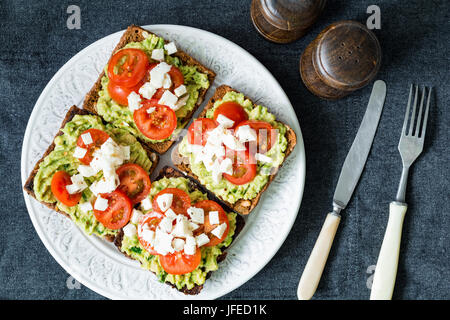 Avocado toast. Healthy toast with avocado mash, cherry tomatoes and crumbled feta cheese on a plate. Table top view Stock Photo