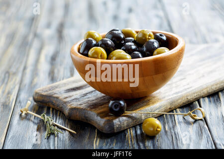 Green and black olives in a wooden bowl. Stock Photo
