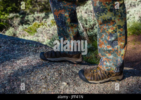 Closeup of man boots and camouflage pants, trousers while hiking on trail in the mountains. Man's hiking shoes and legs closeup outdoors in action. Ve Stock Photo