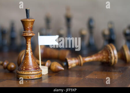 Ancient wooden chess pieces on an old chessboard. With the white flag of surrender. Stock Photo