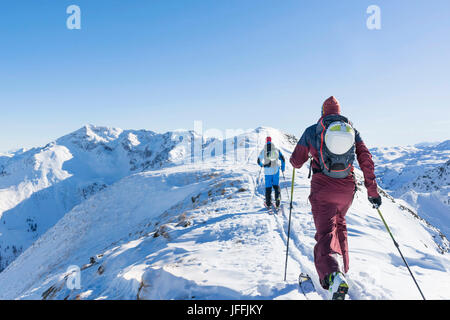 Rear view of skiers walking on ridge of mountain against sky Stock Photo