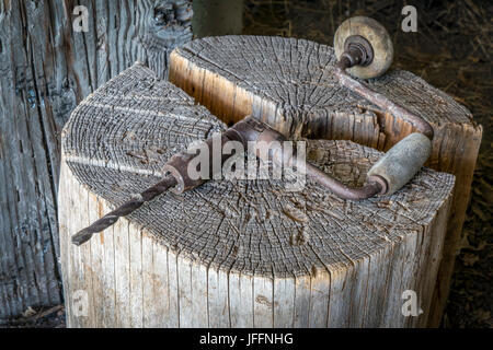 Vintage hand drill on wooden log in an old farm workshop Stock Photo