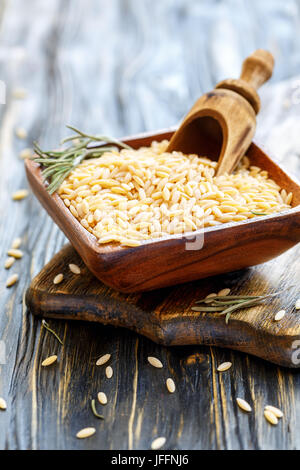 Wooden scoop in bowl of orzo pasta. Stock Photo