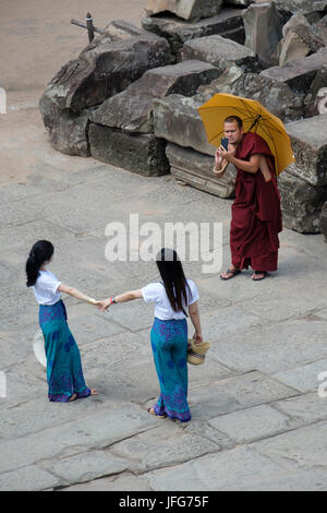 Buddhist monk taking pictures of two girls on holidays using his smartphone while visiting Angkor Wat temple complex in Cambodia, Asia Stock Photo