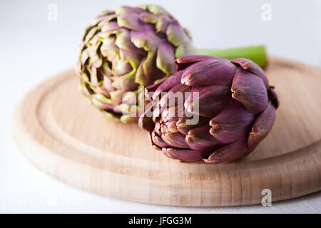Two artichokes lying on a wooden plate Stock Photo