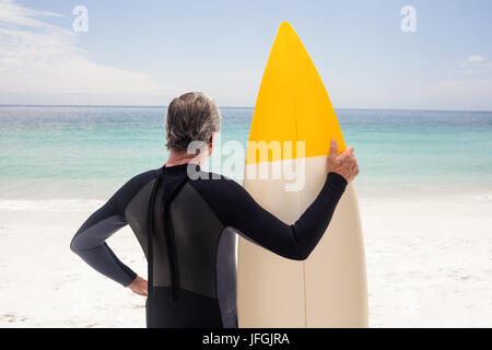 Rear view of senior man in wetsuit holding a surfboard Stock Photo