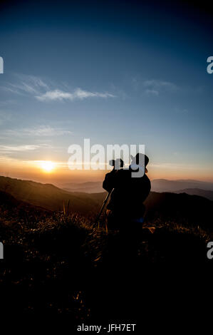 silhouette of photographer taking picture of landscape during sunrise Stock Photo