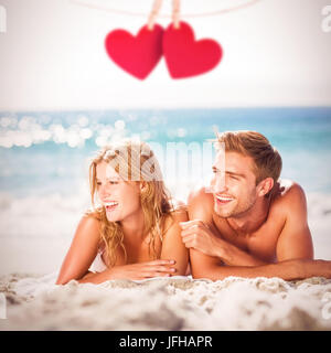 Composite image of happy couple relaxing together in the sand Stock Photo