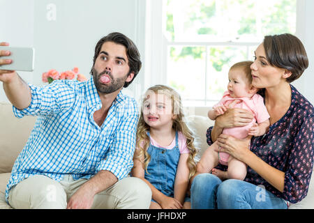 Family making faces while taking selfie on sofa Stock Photo